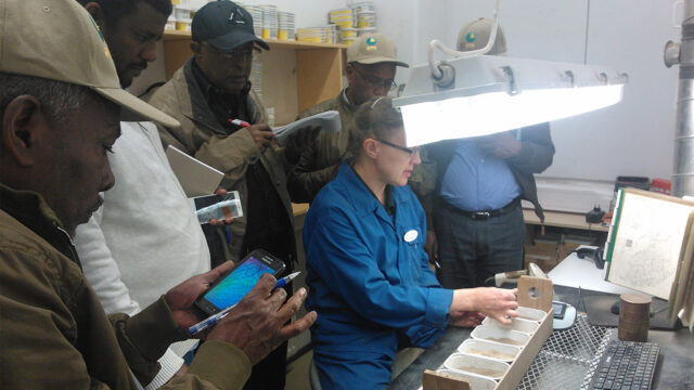 research specimens on the table. A woman teaching and others taking notes and listening.