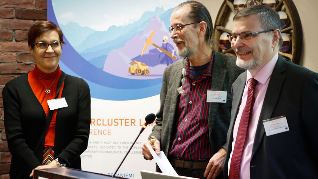 three persons at the event behind the microphone. They are smiling.