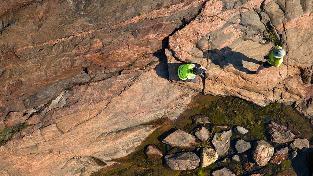 Two people are examining a rock by the sea