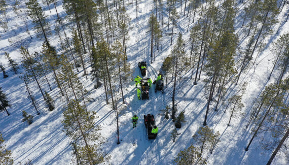 Ylhäältä otettu kuva talvisesta metsästä. Huomiovaatteissa olevat henkilöt tekevät tutkimuksia. Mukana myös kaksi moottoriajoneuvoa.