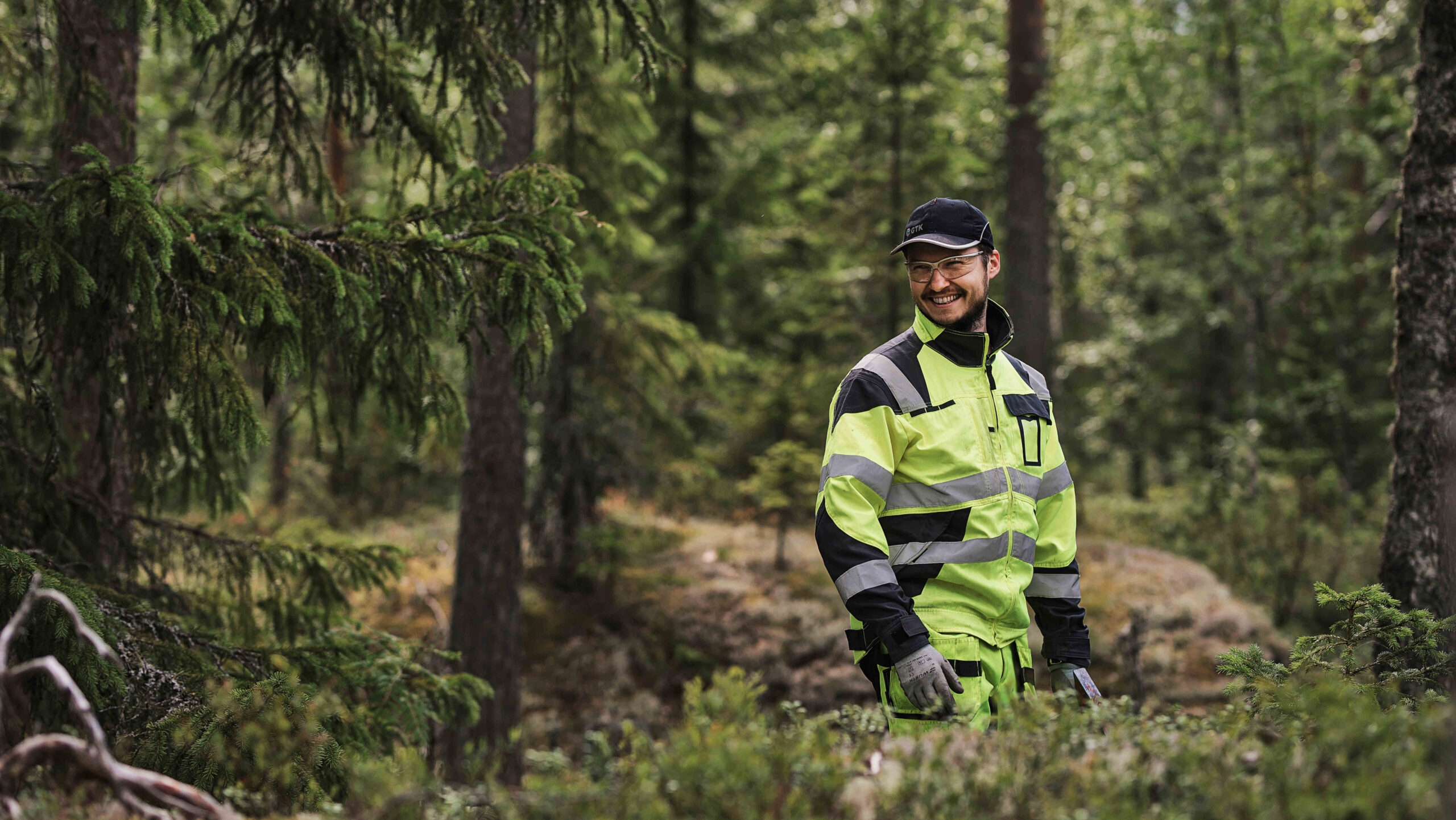 A smiling man in a forest wearing yellow protective gear