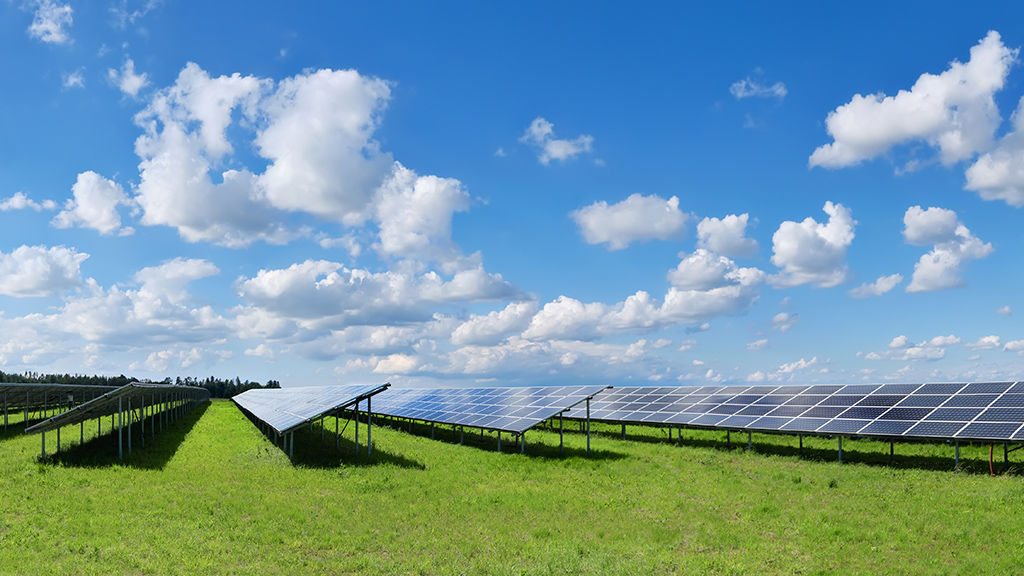 Solar power plant in Autumn. Solar panels on orange grass field under blue sky with clouds