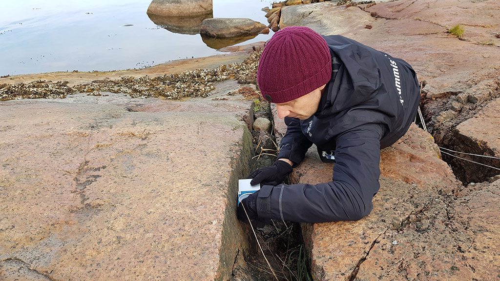 Tutkija aurinkoisena päivänä merenrannan kallioilla ottamassa mittausta.
