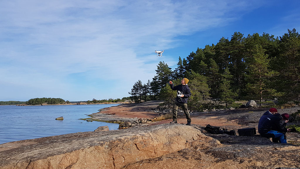 Tutkija aurinkoisena päivänä merenrannan kallioilla lähettämässä drone-mittalaitetta matkaan.