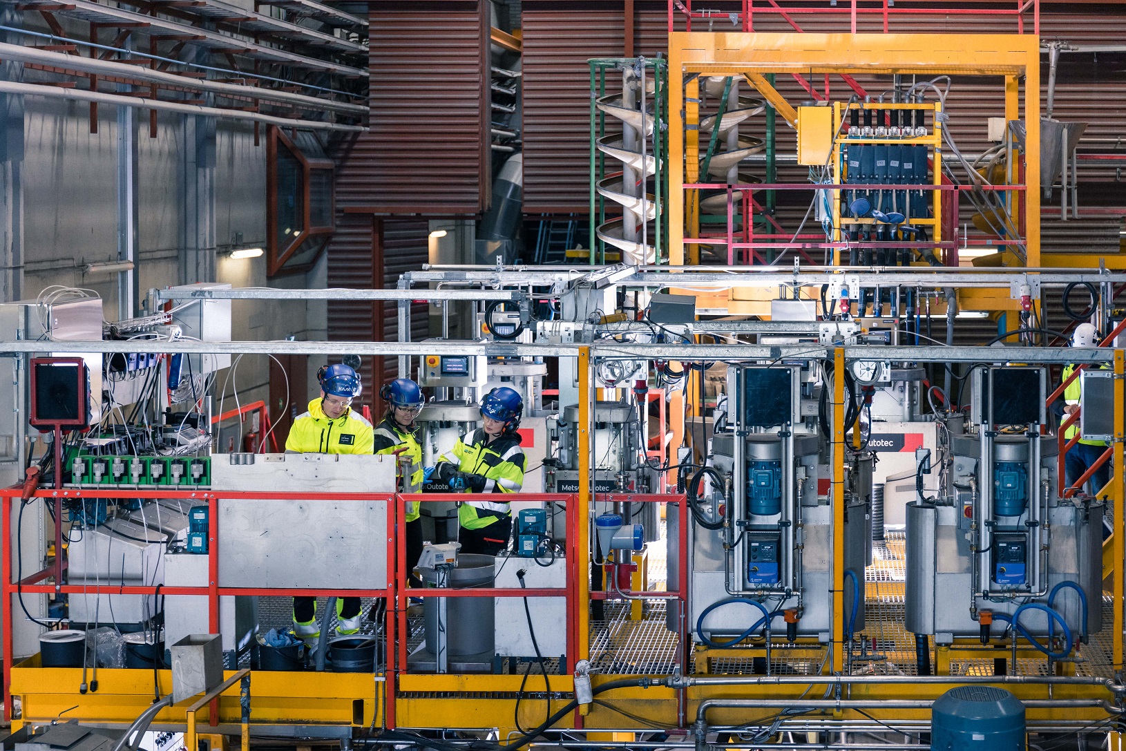 Factory hall. There are 3 persons using equipments with security clothes on.