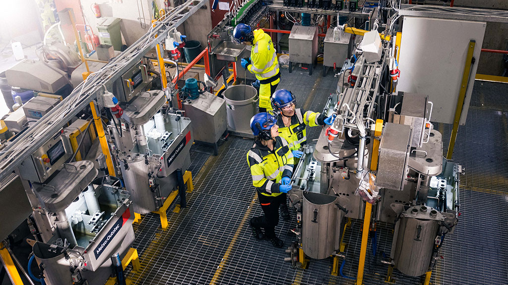 Ylhäältäpäin otettu kuva, jossa 3 henkilöä työskentelevät tehdaskoneiden kanssa.