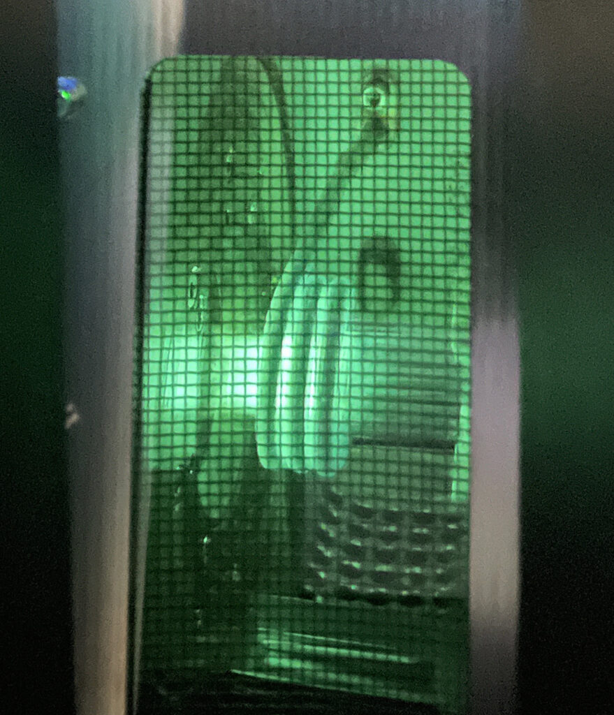 A photo taken from behind a safety glass. Plasma flares are burning green.