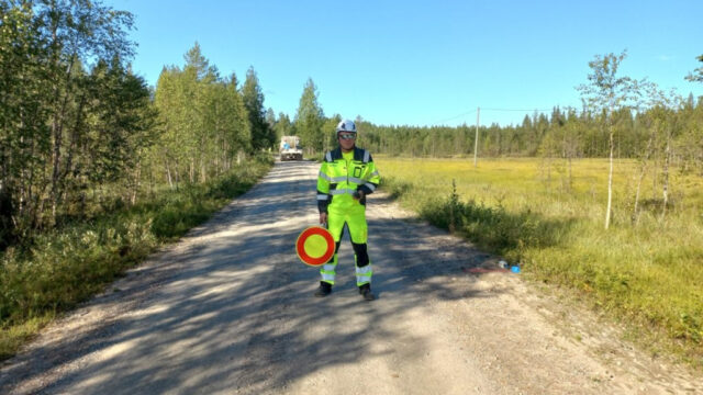 En person klädd i speciella kläder dirigerar trafiken på en skogsväg.