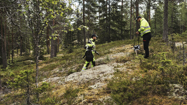 Kaksi henkilöä heijastavissa vaatteissa työskentelee metsässä.