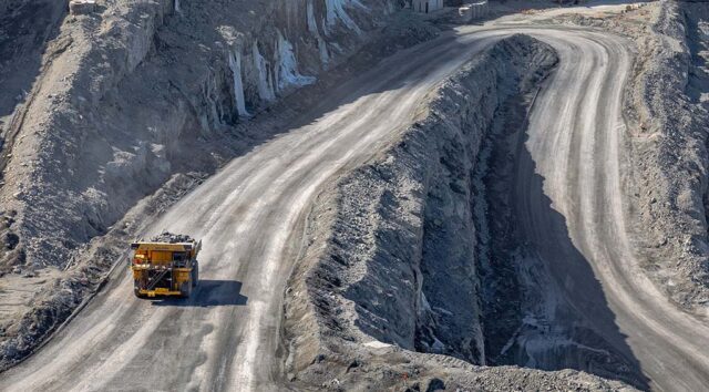 A large truck drives on a winding road in an open-pit mine.